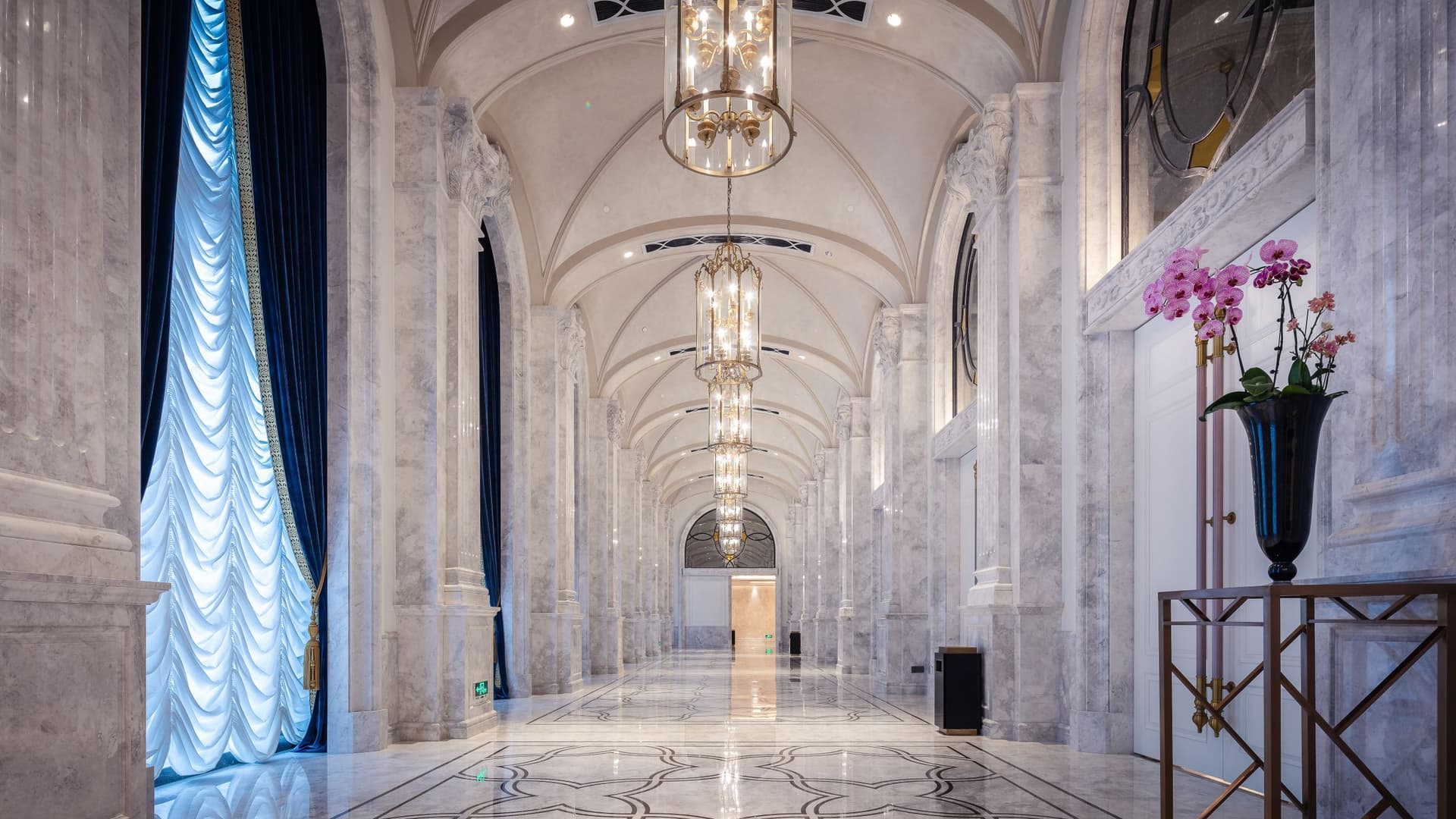 A grand marble hall — marble-clad columns and a patterned marble floor beneath chandeliers.